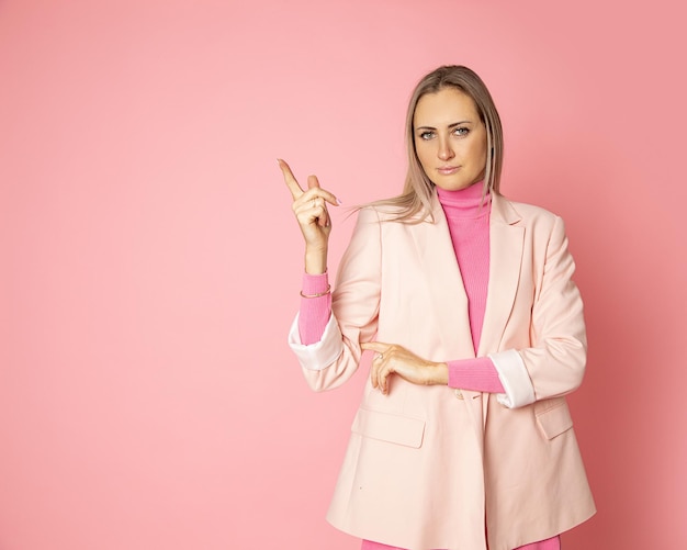 Dama de negocios con cabello rubio dedo señalador en Copyspace sobre fondo rosa en estudio, llamar la atención, concepto de persona de negocios. retrato.