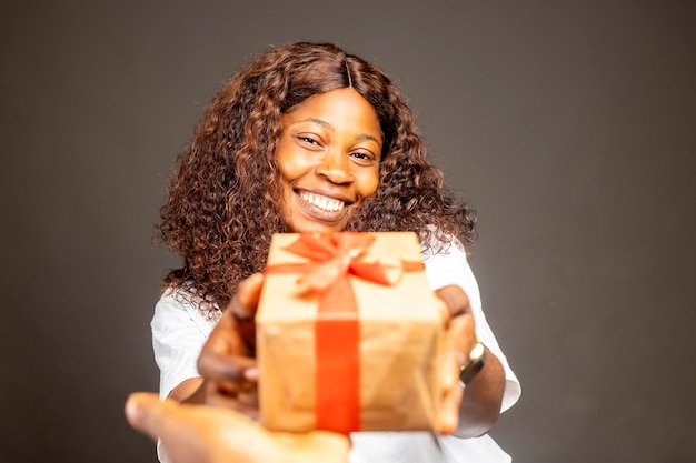 dama negra africana alegre y positiva sosteniendo una caja de regalo envuelta dando un regalo a la cámara de pie