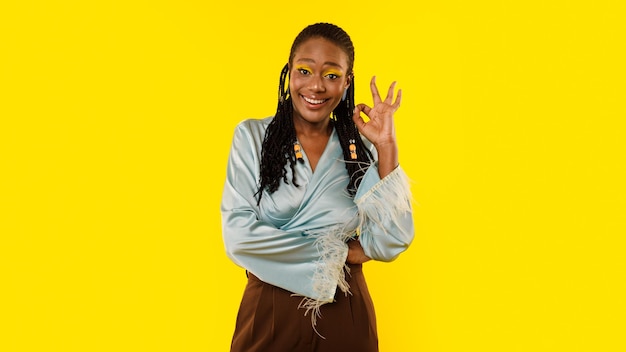Dama negra gesticulando bien símbolo aprobando estilo sobre fondo amarillo