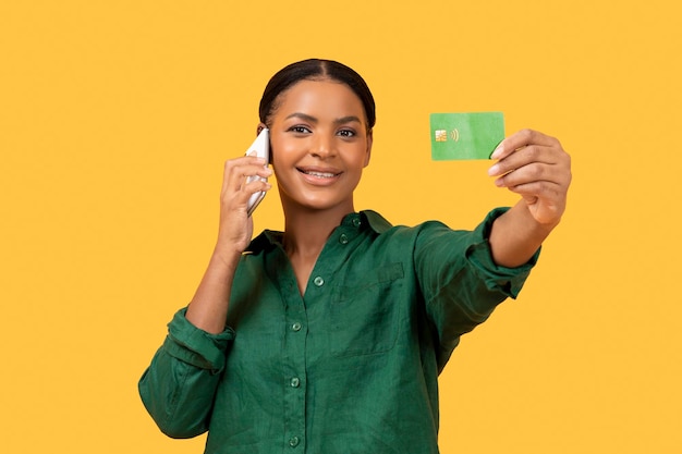 Dama negra hablando por teléfono celular mostrando el fondo amarillo de la tarjeta de crédito