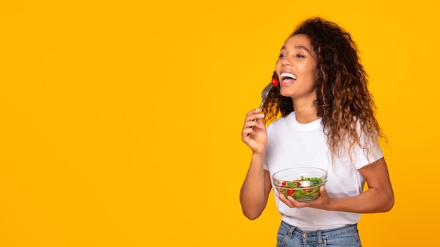 Dama negra del milenio felizmente comiendo ensalada de verduras contra un fondo amarillo