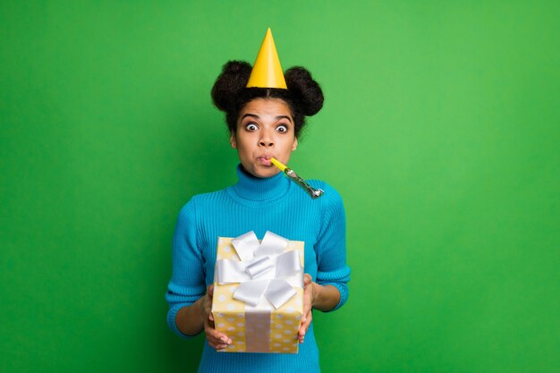 Dama de piel oscura infantil funky sostenga una caja de regalo grande con las manos que soplan hacedor de ruido