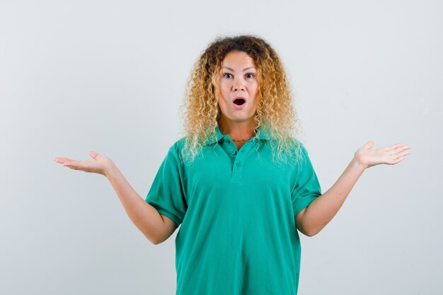 Dama rubia con cabello rizado presentando dos productos, tomados de la mano hacia los lados como si mostrara productos en las palmas de las manos en camiseta verde y pareciendo sorprendida. vista frontal.