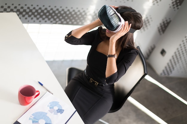 dama en suite fuerte negro sentarse en la mesa de la oficina en gafas vr