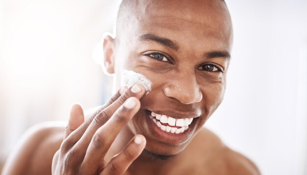 A las damas les encanta un hablador suave con una cara aún más suave Retrato de un joven apuesto que se aplica crema hidratante en la cara en el baño de su casa