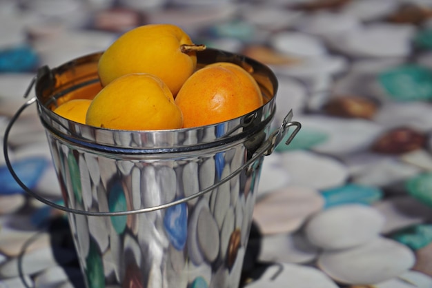 Damascos em um balde decorativo em uma mesa com seixos fotoimpressos