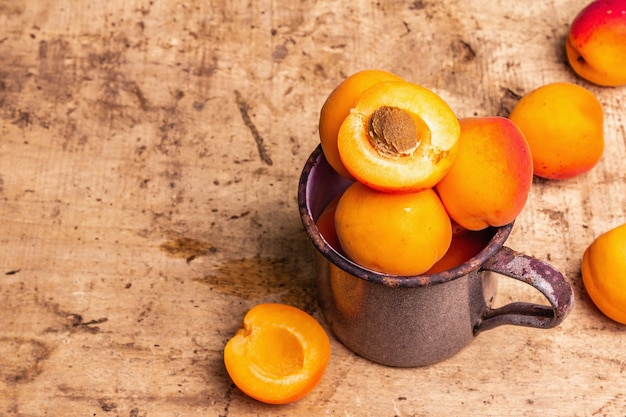 Damascos maduros em uma caneca de ferro vintage. frutas doces, mesa de madeira velha, espaço de cópia