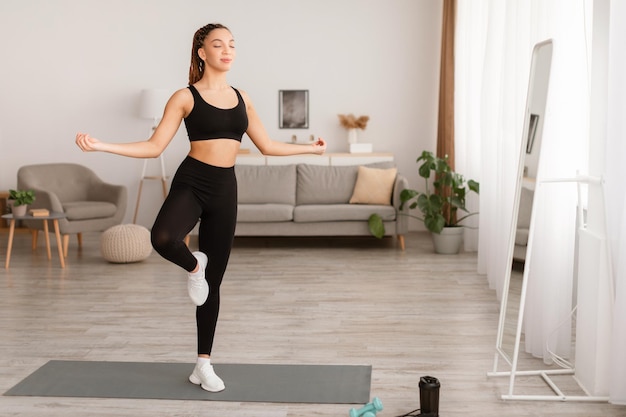 Dame, die in Yoga-Pose auf einem Bein steht und drinnen meditiert