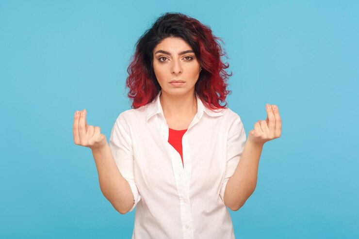 Foto dame dinero en efectivo. retrato de una joven hipster seria con el pelo rojo elegante que muestra un gesto de dinero, pide propinas, paga, exige una recompensa financiera. foto de estudio interior aislado sobre fondo azul.