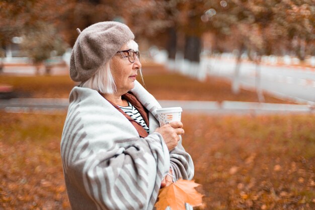 Dame in einer warmen Wolldecke hält eine Pappbecher heißen Tee oder Kaffeegetränk, während sie das genießt