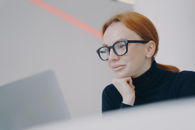 Dame liest auf dem PC-Bildschirm Glückliches Gesicht einer selbstbewussten jungen Frau am Arbeitsplatz in einem modernen Büro