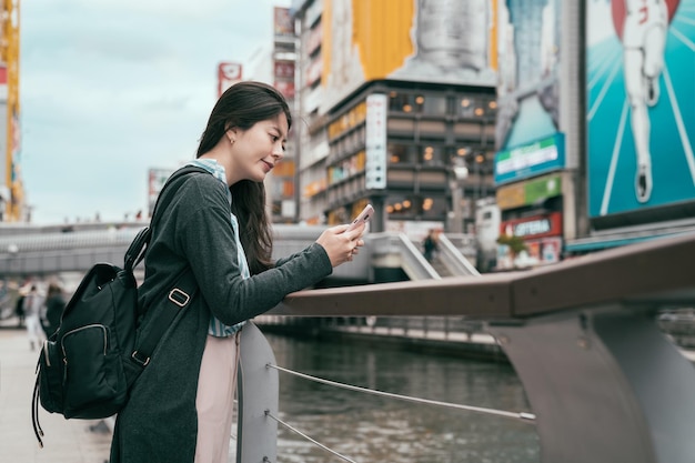 dame reisende mit handy sms sms. junger Rucksacktourist, der sich neben dem Kanal in Osaka verlässt. Schöner Tourist auf dem Handy, der neben dem Fluss plaudert.