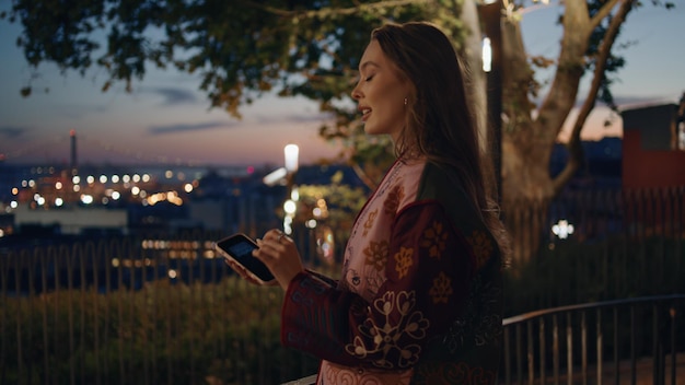 Dame steht auf dem dunkelsten Aussichtsdeck der Stadt mit einem Smartphone in Nahaufnahme, Frau tippt