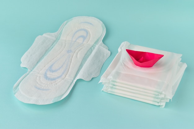 Damenbinde mit einem roten Papierboot auf einem türkisfarbenen Hintergrund. Das Konzept der kritischen Tage, der Menstruation. Gynäkologie. PMS