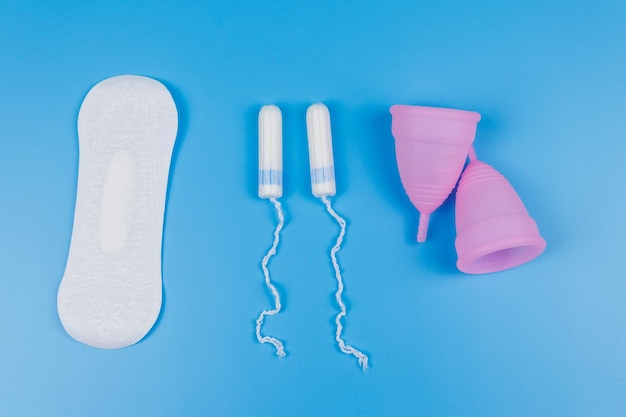 Damenbinde Tampons und Menstruationstasse auf blauem Hintergrund Ansicht von oben Konzept der kritischen Tage Menstruation Damenhygiene