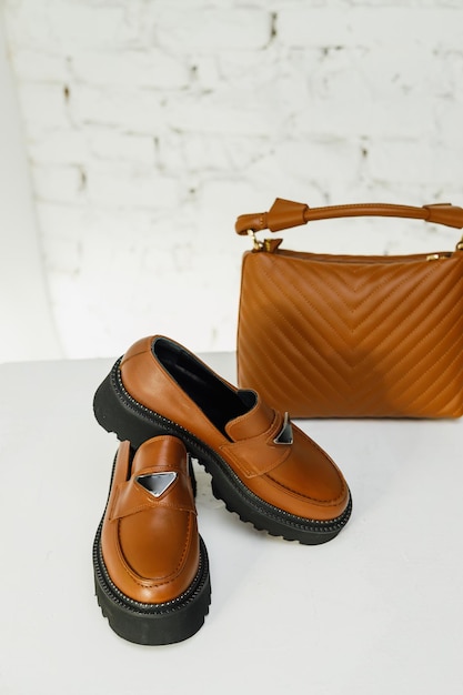 Damenleder stilvolle braune Loafer und braune Handtasche auf weißem Hintergrund Sommerschuhe für Damen Nahaufnahme Modische Schuhe für Frauen Selektiver Fokus