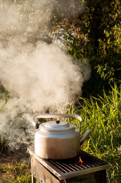 Dampf kommt aus einem Metallkessel, wenn er in der Natur auf dem Grill auf dem Grill mit offenem Feuer erhitzt wird