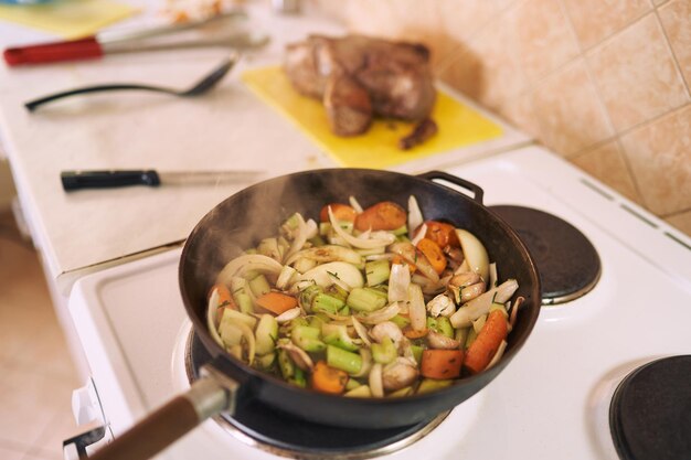 Dampf steigt aus gehacktem Gemüse, das in einer Bratpfanne auf dem Herd gekocht wird