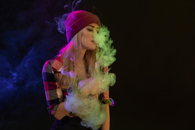 Dampfendes Mädchen. Junge Hipster-Frau vape E-Zigarette auf schwarzem Hintergrund. Hip-Hop-Stil. Dampfkonzept. E-Zigarette dampfen. Studioaufnahme