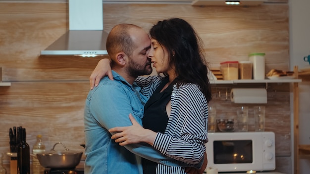 Dança romântica com jantar romântico na cozinha aconchegante. casal feliz e apaixonado jantando juntos em casa, saboreando a refeição, sorrindo, se divertindo, comemorando seu aniversário.