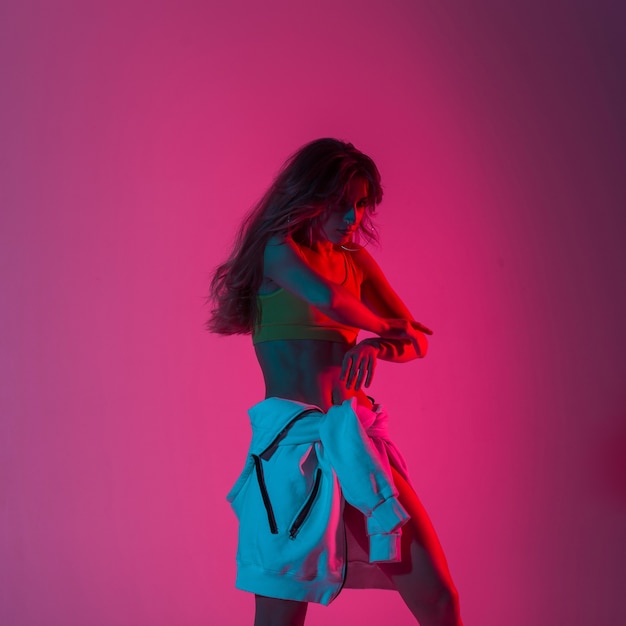 Dançarina bonita na moda jovem com roupas da moda jovem desfrutar de dança no estúdio com fundo de cor rosa. Modelo de moda garota atraente dançando dentro de casa luz neon rosa em estilo discoteca.