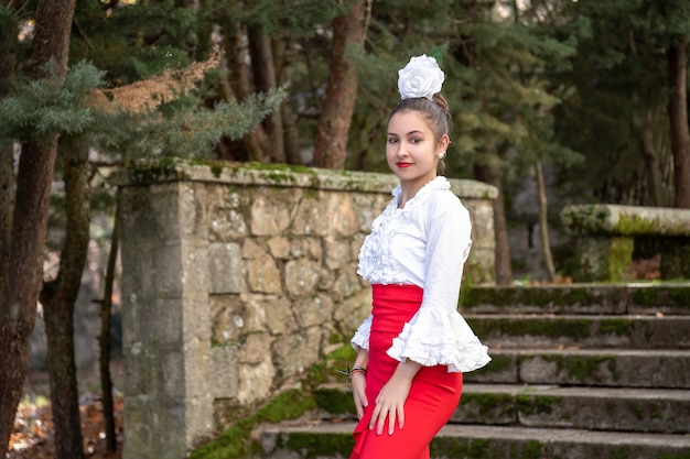 Dançarina de flamenco em um vestido vermelho com camisa e flor branca na cabeça, olhando para a câmera.