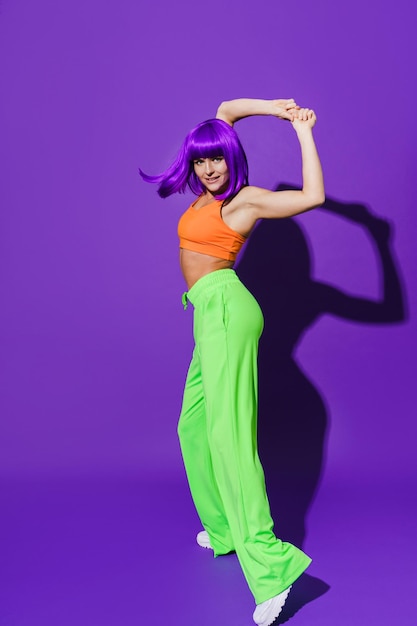 Dançarina despreocupada vestindo roupas esportivas coloridas se apresentando contra o fundo roxo