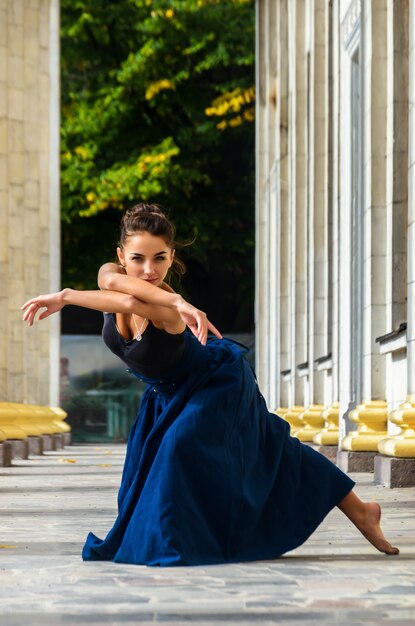 Dançarina linda mulher graciosa em um top preto e uma saia azul longa dança nas ruas da cidade