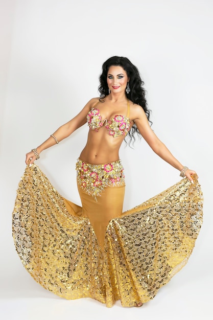 Dançarina Oriental em roupas de cor dourada, com cabelos pretos e pele bronzeada, posando graciosamente de branco