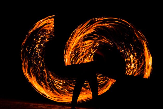 Foto dançarino de fogo masculino em silhueta se apresentando à noite