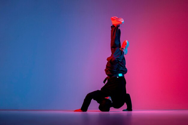 Dançarino fazendo truque acrobático e dançando breakdance em iluminação neon vermelha e azul