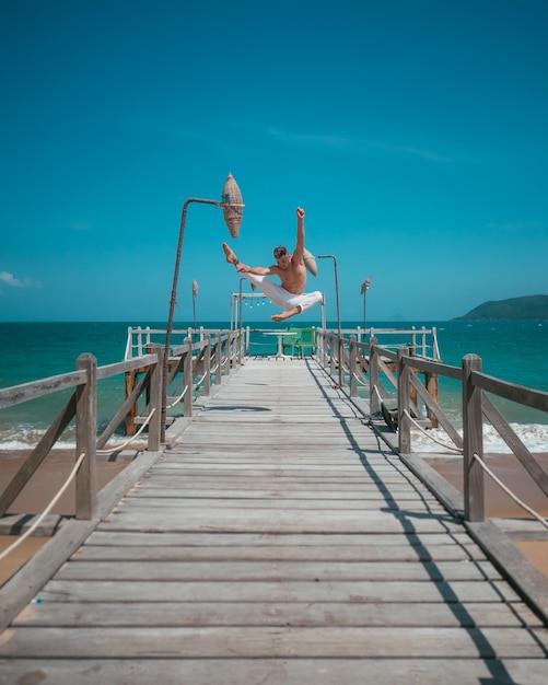 Foto dançarino masculino pulando na ponte de madeira perto do oceano