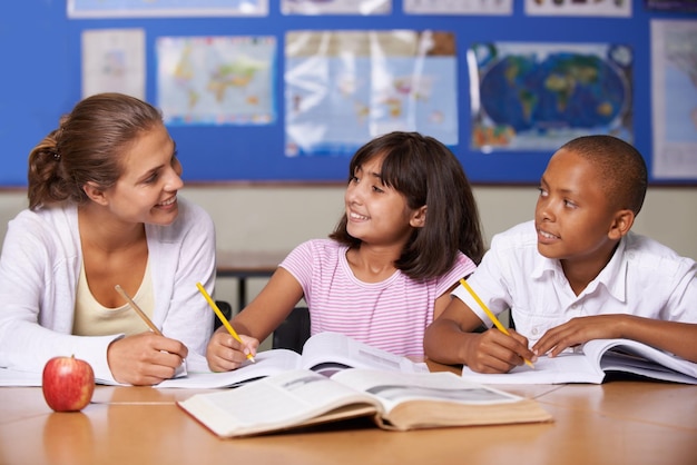 Dando algum reforço positivo uma jovem professora discutindo com seus dois alunos étnicos enquanto eles folheiam um livro didático