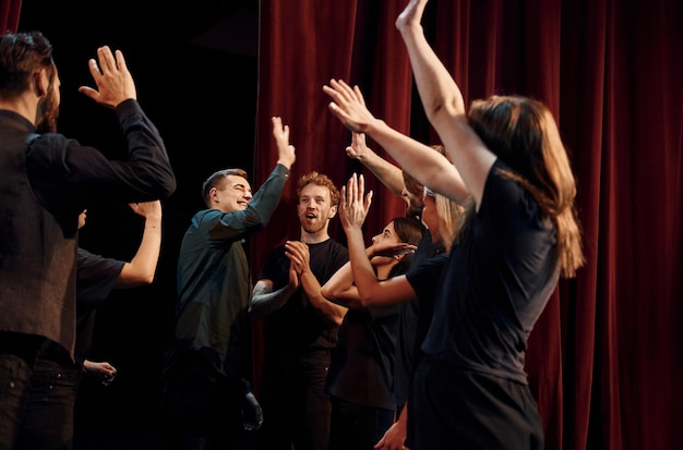 Dando cinco altos celebrando el éxito Grupo de actores en ropa de color oscuro en el ensayo en el teatro