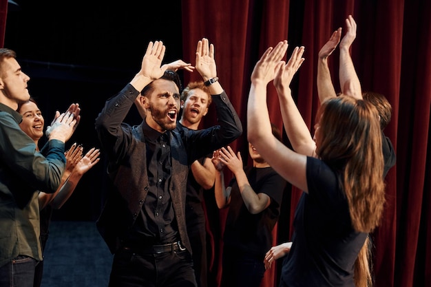 Dando cinco altos celebrando el éxito Grupo de actores en ropa de color oscuro en el ensayo en el teatro