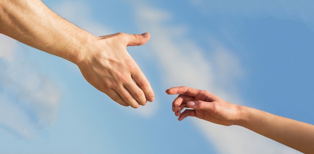 Dando uma mão amiga. Solidariedade, compaixão e caridade, resgate. Mãos de homem e mulher alcançando um ao outro, suporte. Dando uma mão amiga. Mãos de homem e mulher no fundo do céu azul.