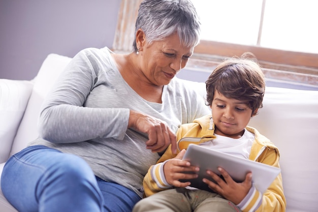 Dándole una lección a la abuela en línea Foto de una abuela y un nieto sentados en casa usando una tableta digital juntos