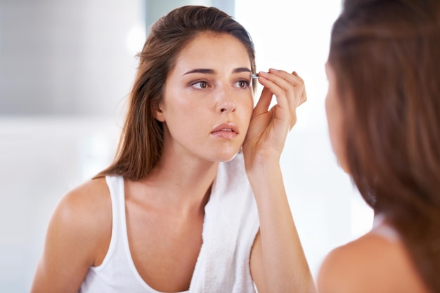 Dándoles forma a la perfección Una mujer joven depilándose las cejas frente a un espejo