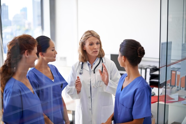 Dándoles sus instrucciones Foto de una doctora asignando tareas a un grupo de enfermeras en un hospital