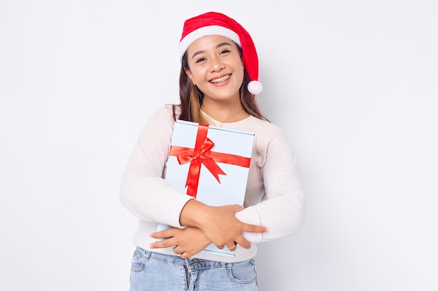 Dankbarkeit und Dank Schöne junge asiatische Frau in einem Sankt-Hut, der eine Geschenkbox trägt, die auf weißem Studiohintergrund lokalisiert wird Frohe Weihnachten-Konzept