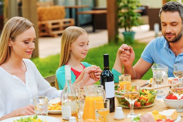 Danke für das Essen. Familie, die Händchen hält und vor dem Abendessen betet, während sie draußen am Tisch sitzt