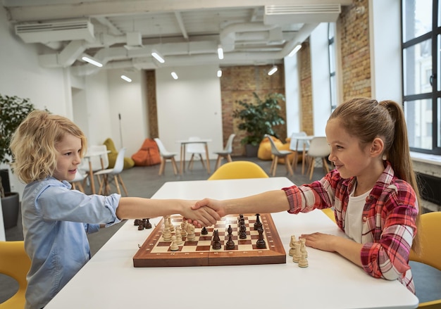 Danke kaukasischer Junge und Mädchen, die sich anschauen und sich die Hände schütteln, nachdem sie Schach gespielt haben