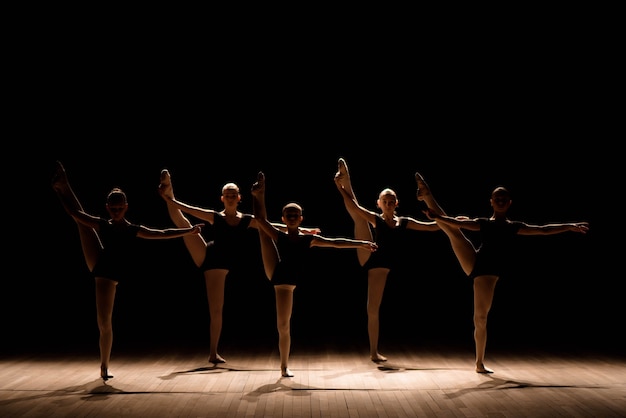 Una danza coreografiada de un grupo de agraciadas bailarinas jóvenes practicando en el escenario de una escuela de ballet clásico.