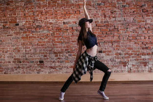 La danza es vida. Estilo de vida hip hop. Felicidad en movimiento, adolescente deportivo sobre fondo de pared de ladrillo con espacio libre. Mujer joven bailando flexible, concepto de breakdance