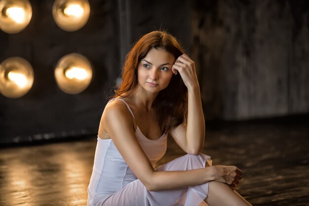 Danza. Joven bailarina bailarina en vestido blanco sentada en el piso de madera