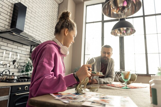 Dar comida. Cuidado padre barbudo dando a su hija plato con comida sentado en la cocina