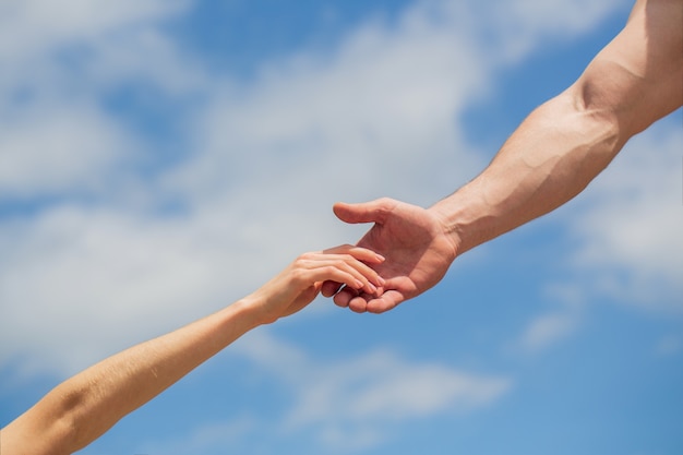 Dar una mano amiga. Manos de hombre y mujer sobre fondo de cielo azul.