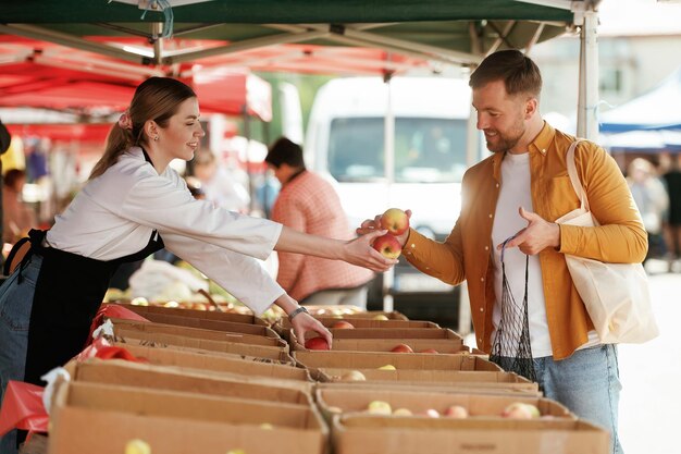 Dar manzanas El hombre está comprando productos en el mercado callejero o bazar de la mujer