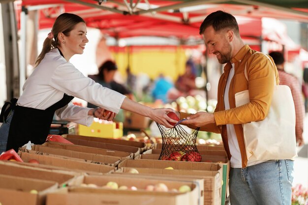 Dar manzanas El hombre está comprando productos en el mercado callejero o bazar de la mujer