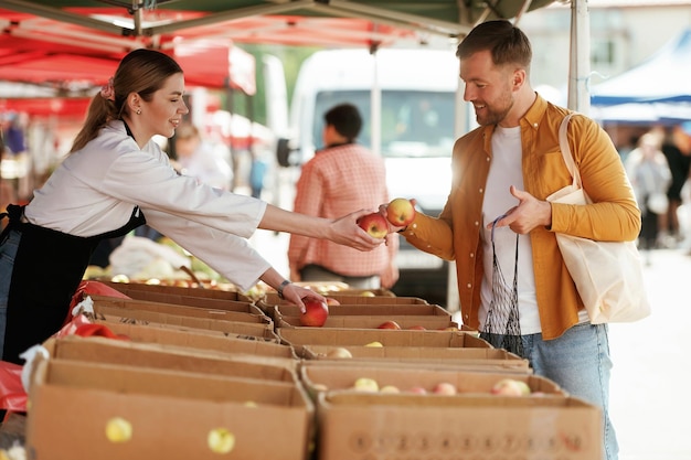 Dar manzanas El hombre está comprando productos en el mercado callejero o bazar de la mujer